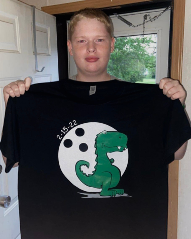 Clayton holds up the shirt that was made by the bowling team, showcasing his one-armed dinosaur.