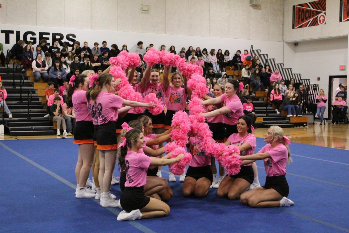The cheerleaders raise their pom poms high to show the Breast cancer ribbon.