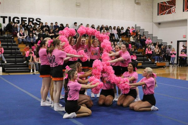 The cheerleaders raise their pom poms high to show the Breast cancer ribbon.